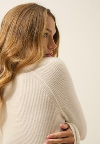 Kremowy sweter z prążkowanego dzianiny z okrągłym dekoltem i długimi rękawami. Teksturowany materiał o przytulnym wyglądzie, z miękkimi, grubymi włóknami.