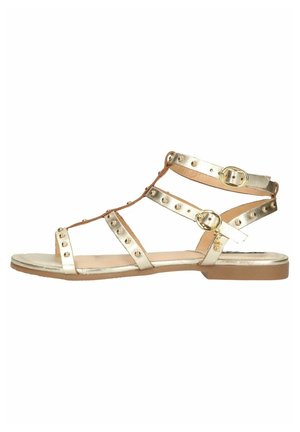 Kultaiset metalliset tasapohjaiset sandaalit, joissa on niitattu remmit, avonainen varvasosa ja nilkkahihnat. Sileä pinta, jossa on ruskea pohja ja matala korko.