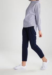 Camicia a righe azzurra e bianca; abbinata a pantaloni tapered blu navy; sneakers bianche con tre strisce sul lato.