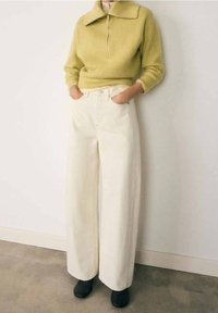 Pull zippé en maille côtelée vert clair avec un grand col, associé à un pantalon large crème taille haute et des chaussures noires.