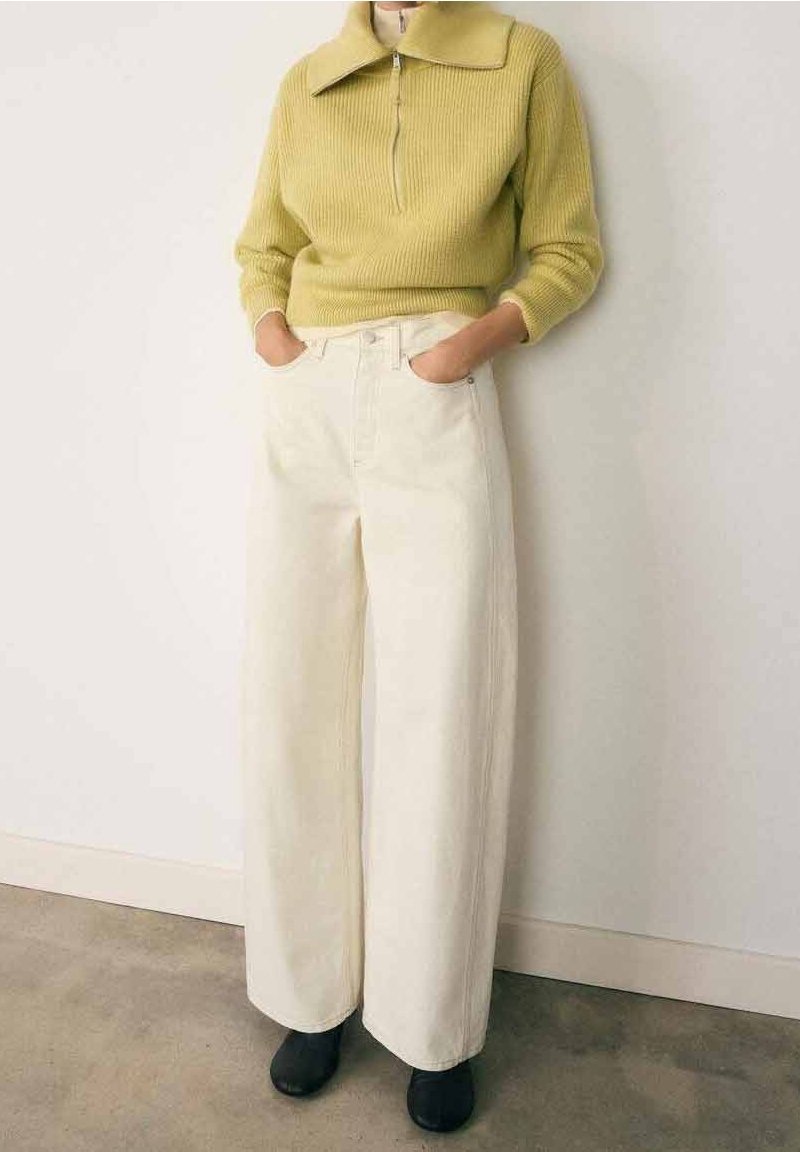 Pull zippé en maille côtelée vert clair avec un grand col, associé à un pantalon large crème taille haute et des chaussures noires.