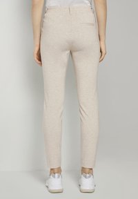 Ljusbeiga elastiska byxor med smal passform, med en enda bakficka och en slät, mjuk tygkvalitet. Kombineras med vita sneakers.