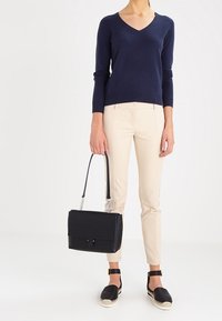 Maglione a V blu navy, pantaloni beige aderenti, borsa nera con manico a catena e espadrillas nere con cinturini alla caviglia.