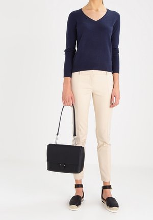 Pull V en navy, pantalon beige ajusté, sac à main noir avec une anse en chaîne, et espadrilles noires avec des brides de cheville.