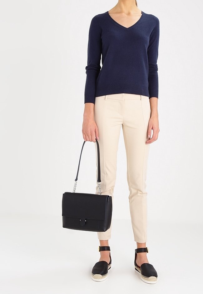 Maglione a V blu navy, pantaloni beige aderenti, borsa nera con manico a catena e espadrillas nere con cinturini alla caviglia.