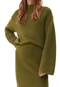 Pull en maille côtelée verte avec un col montant, manches longues et ourlet court ; associé à une jupe ajustée assortie. Tissu texturé à rayures horizontales.