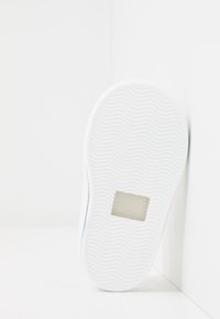 Valge tennisekinga talla laineline tekstuur, millel on ristkülikukujuline silti, millel on reljeefne tekst "MADE IN SPAIN". Sujuv ja puhas disain.