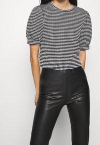 Černobílý top s kostkovaným vzorem houndstooth, krátkými Puff rukávy a kulatým výstřihem, doplněný o lesklé černé upnuté kalhoty.