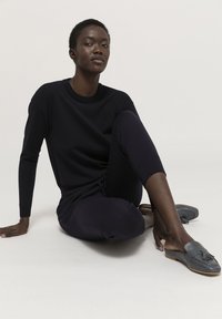 Dunkelblauer Strickpullover mit langen Ärmeln, kombiniert mit dunkelblauen Jogginghosen. Graue Slipper mit Quasten-Detail. Glatte Textur.