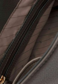 Interno della borsa in pelle marrone con un rivestimento morbido a strisce sottili e una tasca con zip per la conservazione. Gli accessori sono di un dorato metallico.