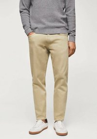 Pantalones de algodón beige con corte recto, que cuentan con bolsillos laterales y una textura suave, combinados con zapatillas blancas y un suéter gris.