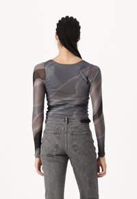 Bluza gri, cu maneci lungi, translucentă, cu un model abstract și un design ajustat; asociată cu blugi gri texturați, cu talie înaltă.