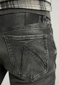 Mörkgrå denimjeans har en unik design på bakfickan med kontrasterande sömmar och en läderpatch med texten "CHASING."