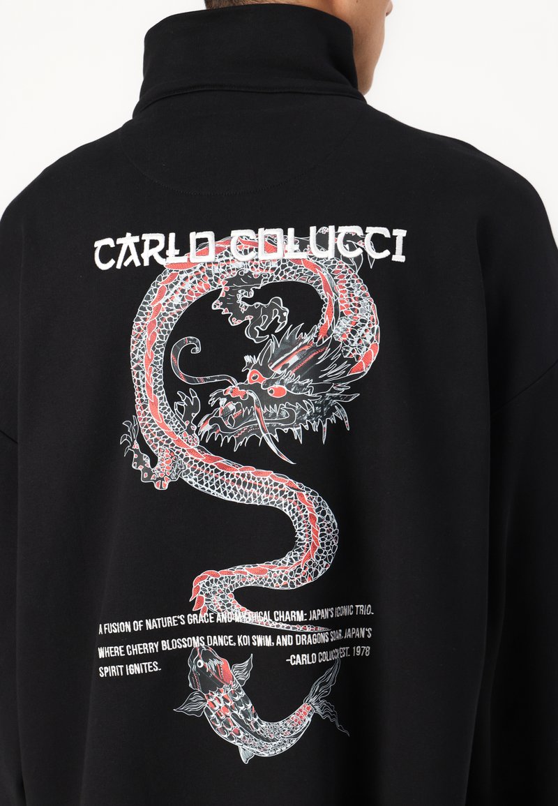 Zwart sweatshirt met hoge kraag, voorzien van een rode en witte draakillustratie op de achterkant en tekst eronder. Katoenen stof, relaxed fit.