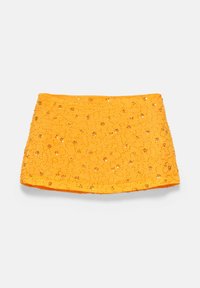 Mini-jupe jaune décorée de petites paillettes et de motifs floraux en perles sur un fond blanc uni.