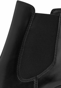 Bottine noire avec un corps en cuir lisse et des panneaux latéraux en élasthanne. Le design comprend des détails cousus et une finition mate.