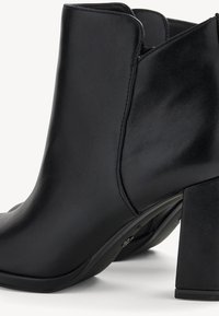 Zwarte enkellaars gemaakt van glad nep leer; voorzien van een blokhak, afgeronde neus en naaddetails.