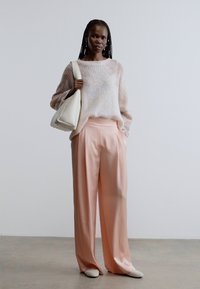 Pull rose clair en maille avec une coupe décontractée ; Pantalon ample et fluide couleur pêche ; Sac blanc ; Tissus doux et texturés ; Design minimaliste.