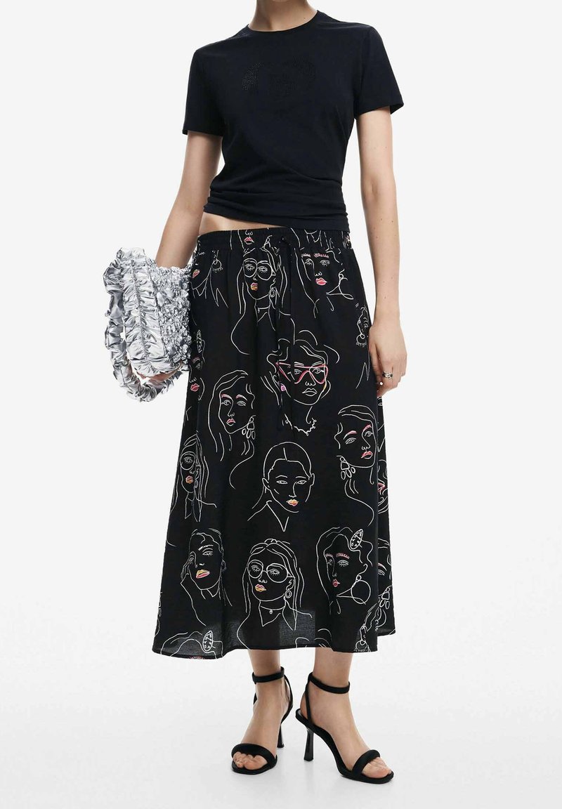 Jupe noire avec des illustrations de visages abstraits blancs et colorés, associée à un t-shirt noir ajusté et des sandales à talons hauts noires à lanières.