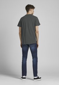 Camiseta de algodón gris con mangas cortas y un ajuste relajado, combinada con jeans de mezclilla azul oscuro y zapatillas negras. Diseño minimalista.