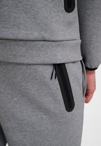 Sivi dukserica i trenirke od mekanog materijala, s crnim patentnim zatvaračem i kontrastnim crnim dizajnerskim detaljima. Teksturirana površina.