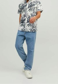 Camicia a maniche corte con motivo di foglie nere su sfondo bianco, abbinata a jeans a gamba dritta azzurri e scarpe da ginnastica bianche.