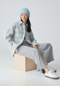 Veste en laine mélangée à rayures bleu clair, pantalon large gris, baskets blanches avec accents gris, et un bonnet en tricot bleu clair assorti.