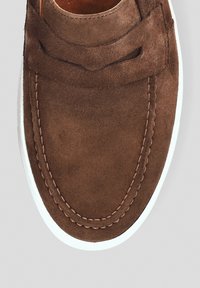 Brązowy zamszowy but z zaokrąglonym noskiem, ozdobnym przeszyciem i białą gumową podeszwą. Gładka faktura, design typu wsuwany, bez widocznych elementów metalowych.