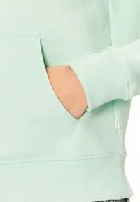 Felpa verde menta con tasca a marsupio, polsini e orlo ribattuti. Tessuto morbido, con un piccolo tag di branding sul lato.