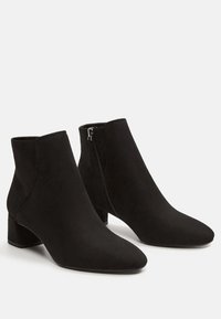 Bottines en suède noir avec talons bloc et fermetures éclairs sur les côtés, présentées sur un fond blanc.