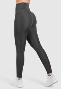 Leggings neri a vita alta realizzati in un tessuto elasticizzato, con una superficie liscia, design aderente e tasche laterali per una maggiore funzionalità.