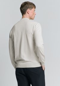 Lichtbeige gebreide trui met een ronde hals, lange mouwen en geribbelde manchetten, met een textuurafwerking op de achterkant en een eenvoudig ontwerp.