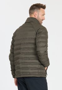 Mørkeolivenfarvet pufferjakke med en lynlåslomme i siden, prydet med et quiltet design og en høj krave. Blød, glat tekstur.