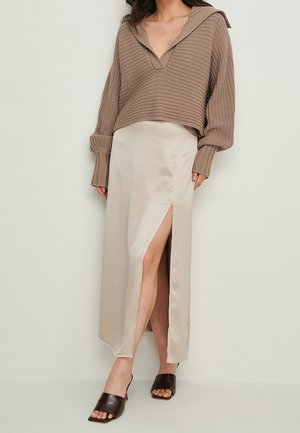 Femme portant un pull en maille taupe avec capuche, une jupe en satin beige fendue haute et des mules ouvertes à talons brun foncé.