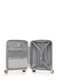 Twarda walizka w kremowym kolorze o teksturowanym wykończeniu. Wnętrze wyposażone w szarą podszewkę, kieszenie zapinane na zamek oraz regulowane paski do zabezpieczania rzeczy.