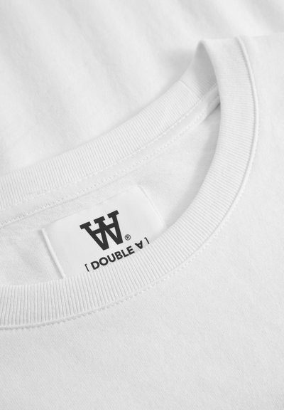 Biela bavlnená tričko s okrúhlym výstrihom a pružným lemovaním; obsahuje čiernu štítku s logom "[ DOUBLE A ]" na vnútornej strane výstrihu.