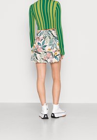 Grön- och vitrandig långärmad topp i kombination med en blommönstrad, lager på lager kjol i rosa och grönt, kompletterad med vita ankelskor.