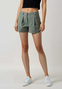 Shorts à carreaux verts avec des plis, dotés d'une fermeture à bouton, de poches et d'un design ajusté, associés à des baskets blanches.