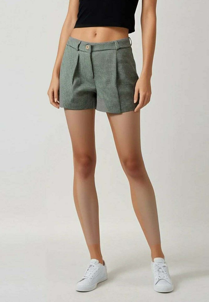 Shorts à carreaux verts avec des plis, dotés d'une fermeture à bouton, de poches et d'un design ajusté, associés à des baskets blanches.