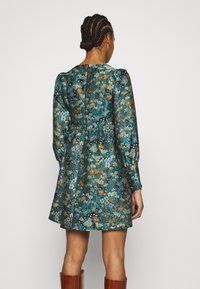 Blumendruckkleid in Teal mit langen Ärmeln, einer gerafften Taille und einem Knopfverschluss auf der Rückseite. Das Muster enthält orangefarbene und gelbe Akzente.