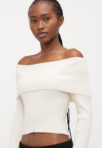 Ecrufarbener, gerippter, verkürzter Pullover mit schulterfreiem Design und langen Ärmeln. Weicher Stoff mit figurschmeichelnder Silhouette.