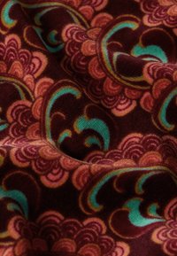 Tessuto con uno sfondo marrone scuro caratterizzato da motivi vorticosi in rosa, pesca e turchese. Texture morbida, pieghe che mettono in risalto i dettagli del design.