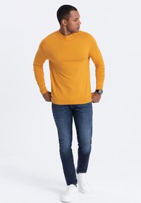 Long-sleeve, crew-neck sweater in bright yellow, paired with dark blue slim-fit jeans and white sneakers. Minimalist design, smooth texture.