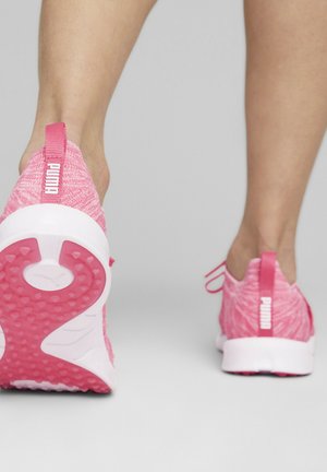 Person wearing bright pink Puma sneakers, showing one shoe’s textured sole and heel logo against a plain background.