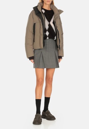 Giacca imbottita di colore marrone chiaro con accenti neri, abbinata a una gonna plissettata grigia. Maglione testurizzato con motivo a rombi. Indossate scarpe chunky.