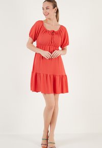 Short red dress with a square neckline, puff sleeves, drawstring detail, and tiered ruffle hem. Made from lightweight, textured fabric.