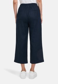 Pantaloni ampi in lino blu navy con vita elasticizzata, due tasche posteriori e una vestibilità rilassata, indossati con sneakers bianche.