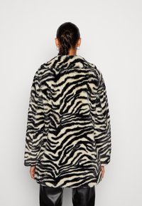 Faux pelsfrakke med et sort og creme zebra mønster, der har en notched krave, lange ærmer og en afslappet pasform.