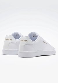 Baskets blanches Reebok avec tige synthétique lisse, col rembourré, semelle extérieure blanche plate et logo doré sur le côté et le talon. Design simple et moderne.