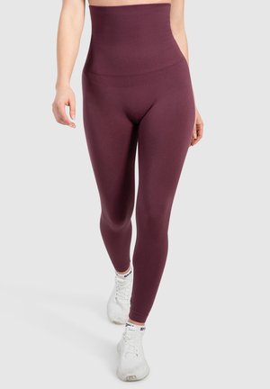  Hooggetailleerde leggings in diep bordeaux, gemaakt van rekbare stof. Gladde textuur, aansluitend ontwerp, gecombineerd met witte sportschoenen.